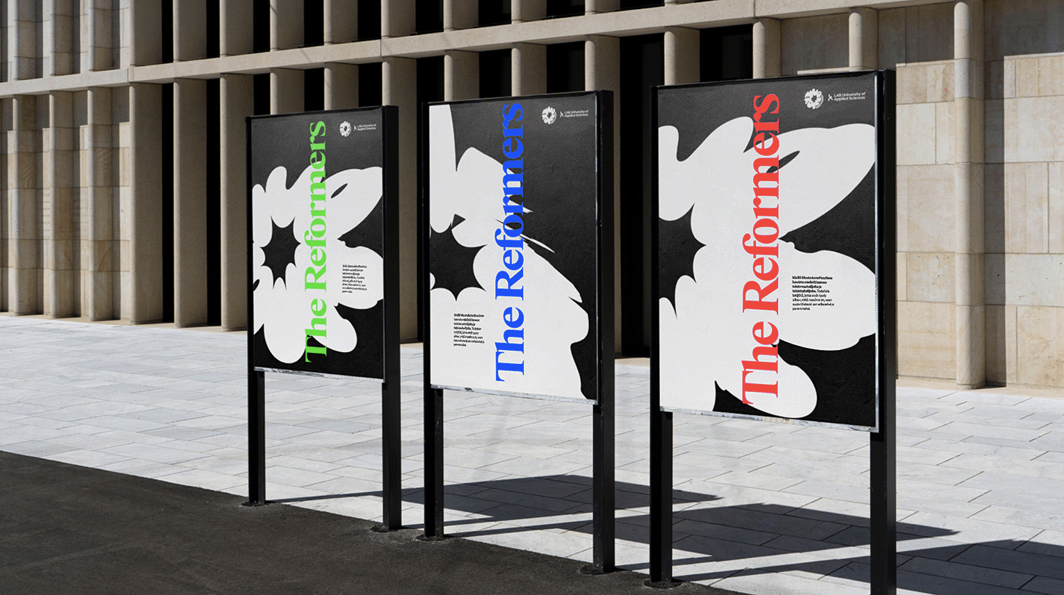 Three black upright display stands showing bold graphic posters with white floral shapes and coloured typography.