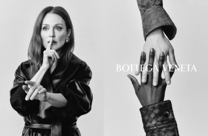 Monochrome ad campaign image featuring Julianne Moore holding a finger to her lips alongside interlocked hands wearing woven leather sleeves.