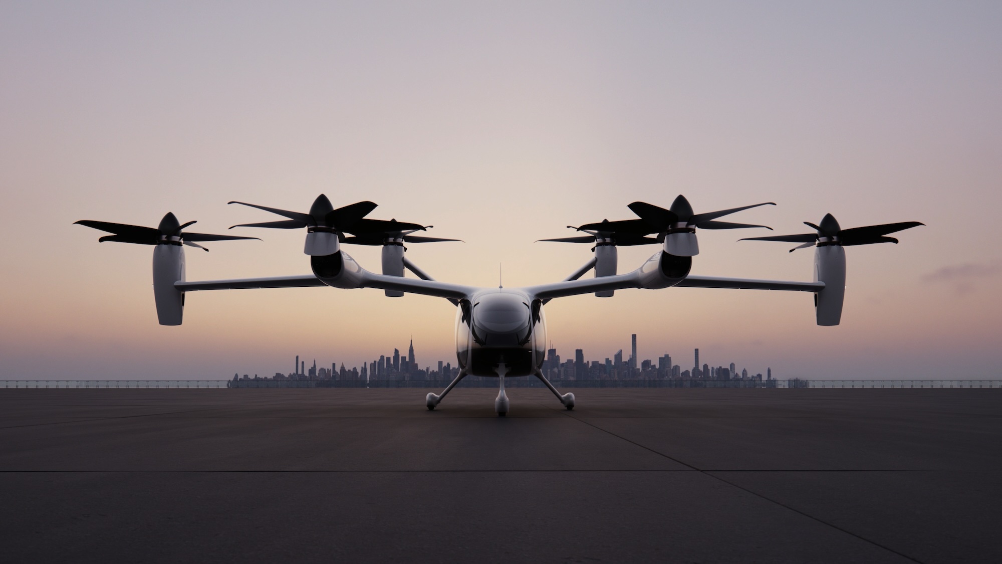 Joby Aviation electric aircraft parked on tarmac facing forward with distant city skyline under sunset sky