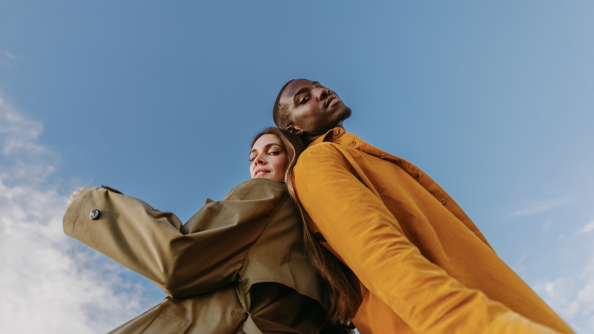 Two people standing back to back against a clear blue sky, viewed from a low-angle perspective.