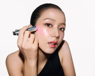 Jisoo applying pink blush with a silver cosmetic stick against a clean white background for Dior