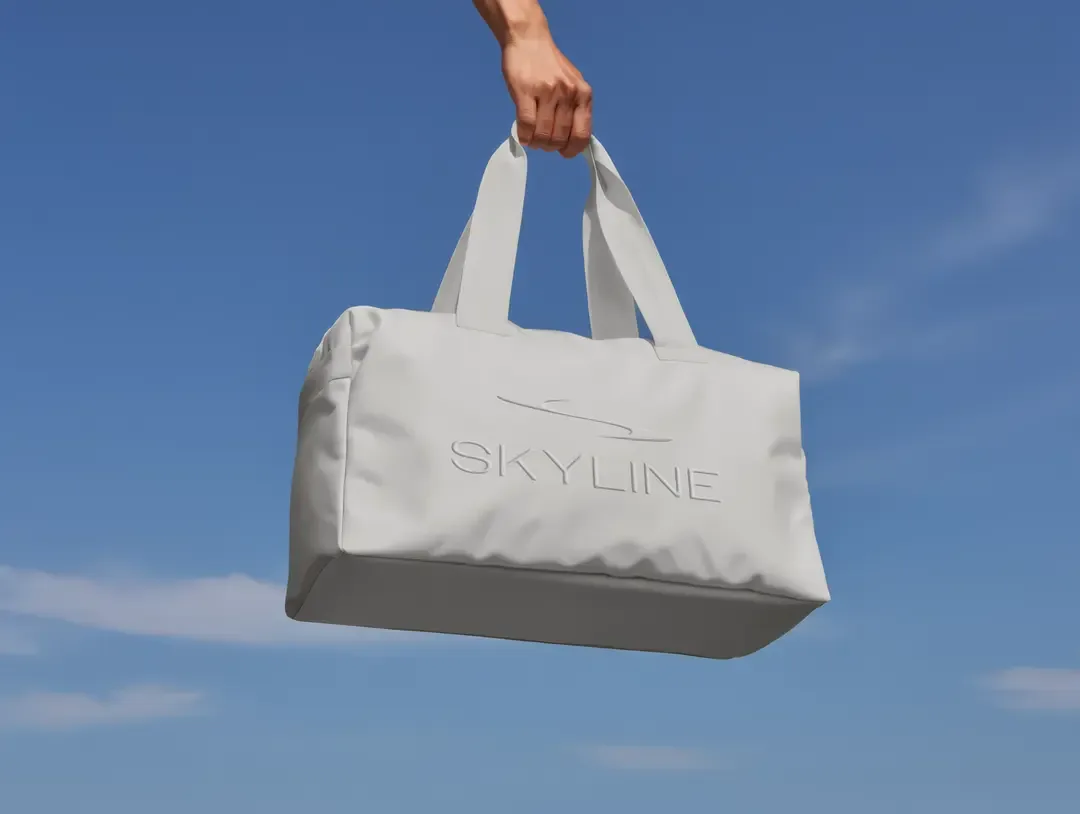 Hand holding a white duffel bag against a bright blue sky background