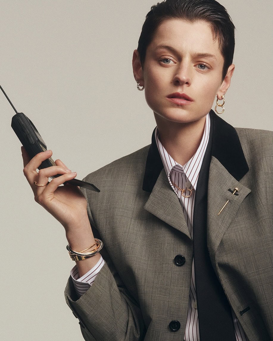 Emma Corrin wearing a grey blazer and holding a vintage mobile phone for Cartier Juste un Clou campaign.