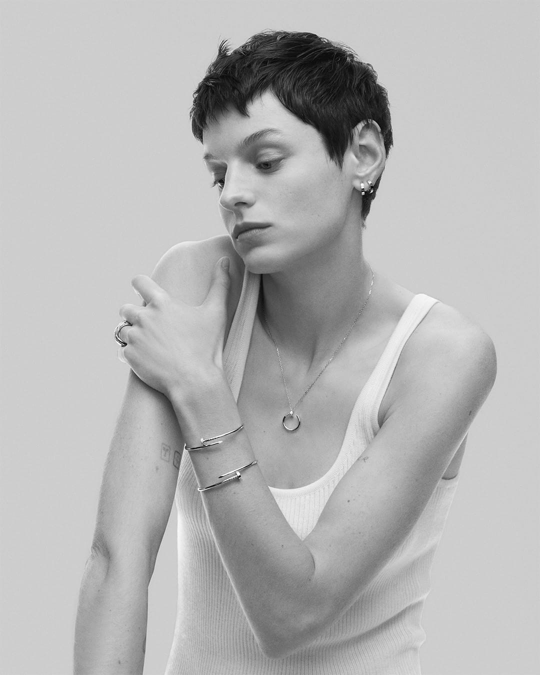 Monochrome portrait of Emma Corrin wearing Cartier Juste un Clou bracelets and pendant necklace against a plain grey backdrop.