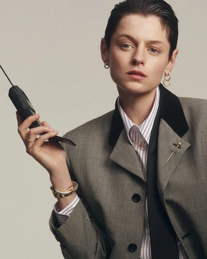 Emma Corrin wearing a grey blazer and holding a vintage mobile phone for Cartier Juste un Clou campaign.