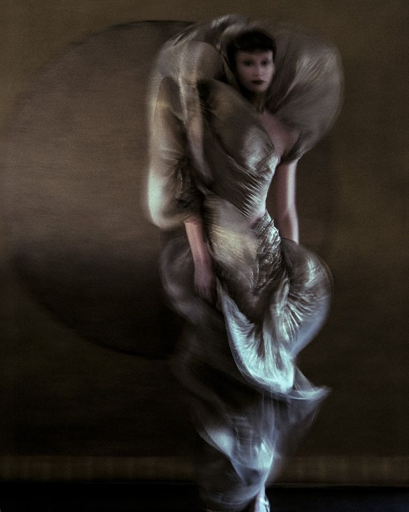 Woman in shimmering haute couture gown with flowing fabric, captured in a studio environment with motion blur, creating a dynamic, artistic effect.
