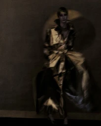 Model wearing a lustrous metallic gold trench coat against a dark textured background in an editorial fashion photograph.