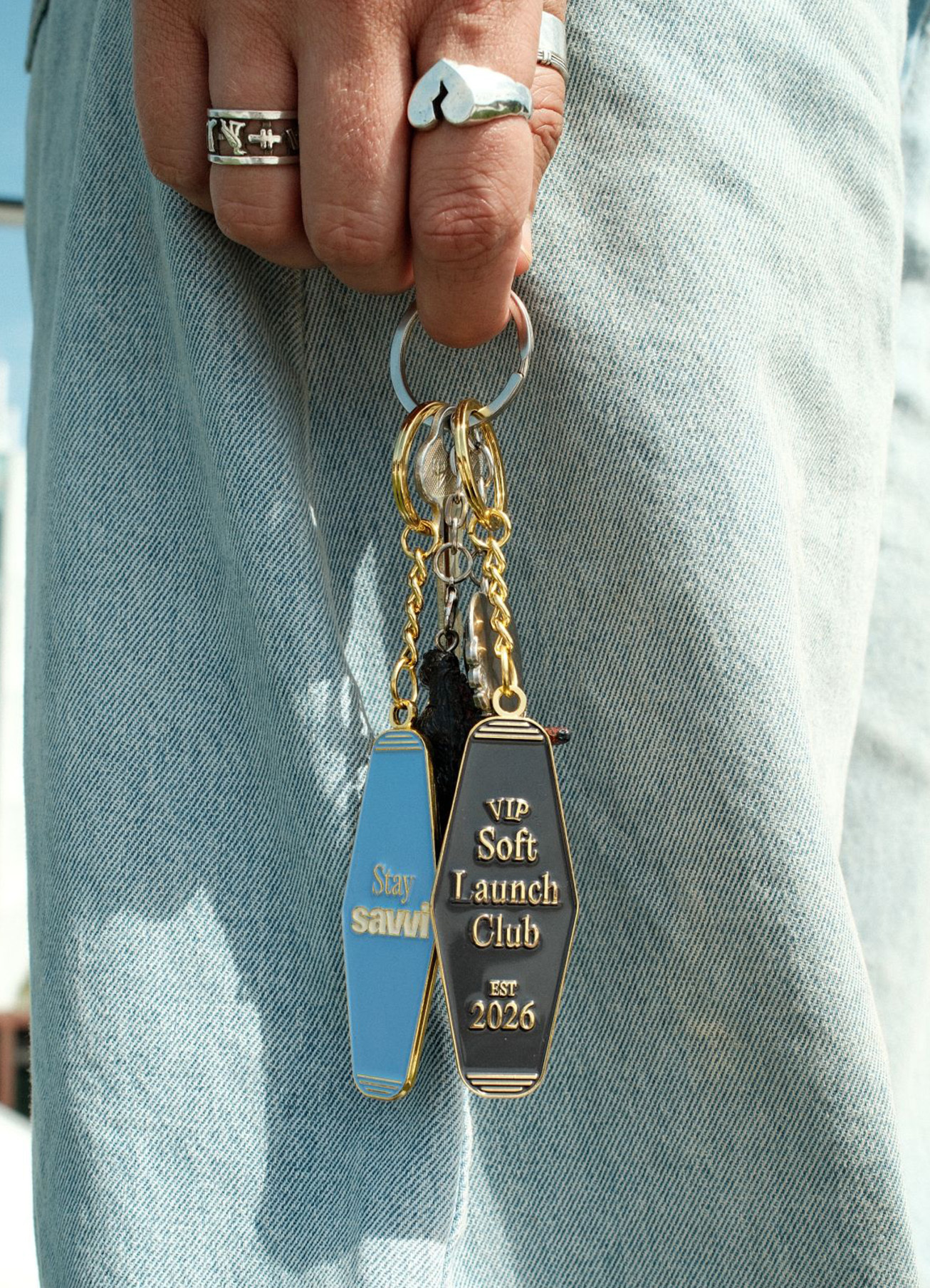 Close-up of a person holding a keyring with custom motel-style keychains against light wash denim jeans