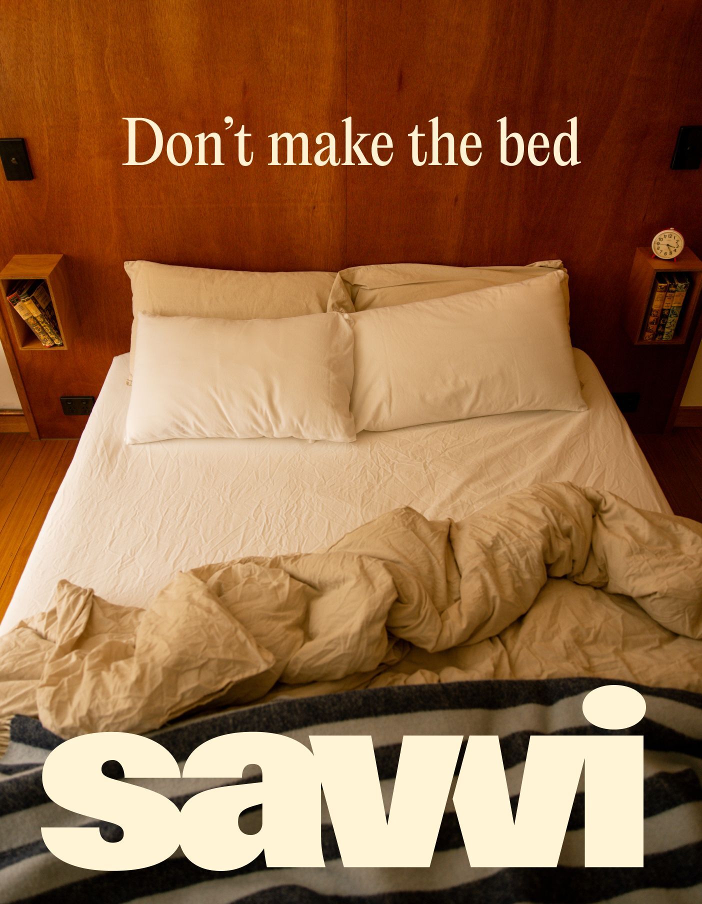 Overhead view of an unmade double bed with white pillows and beige duvet against a wood paneled headboard with built in nightstands.
