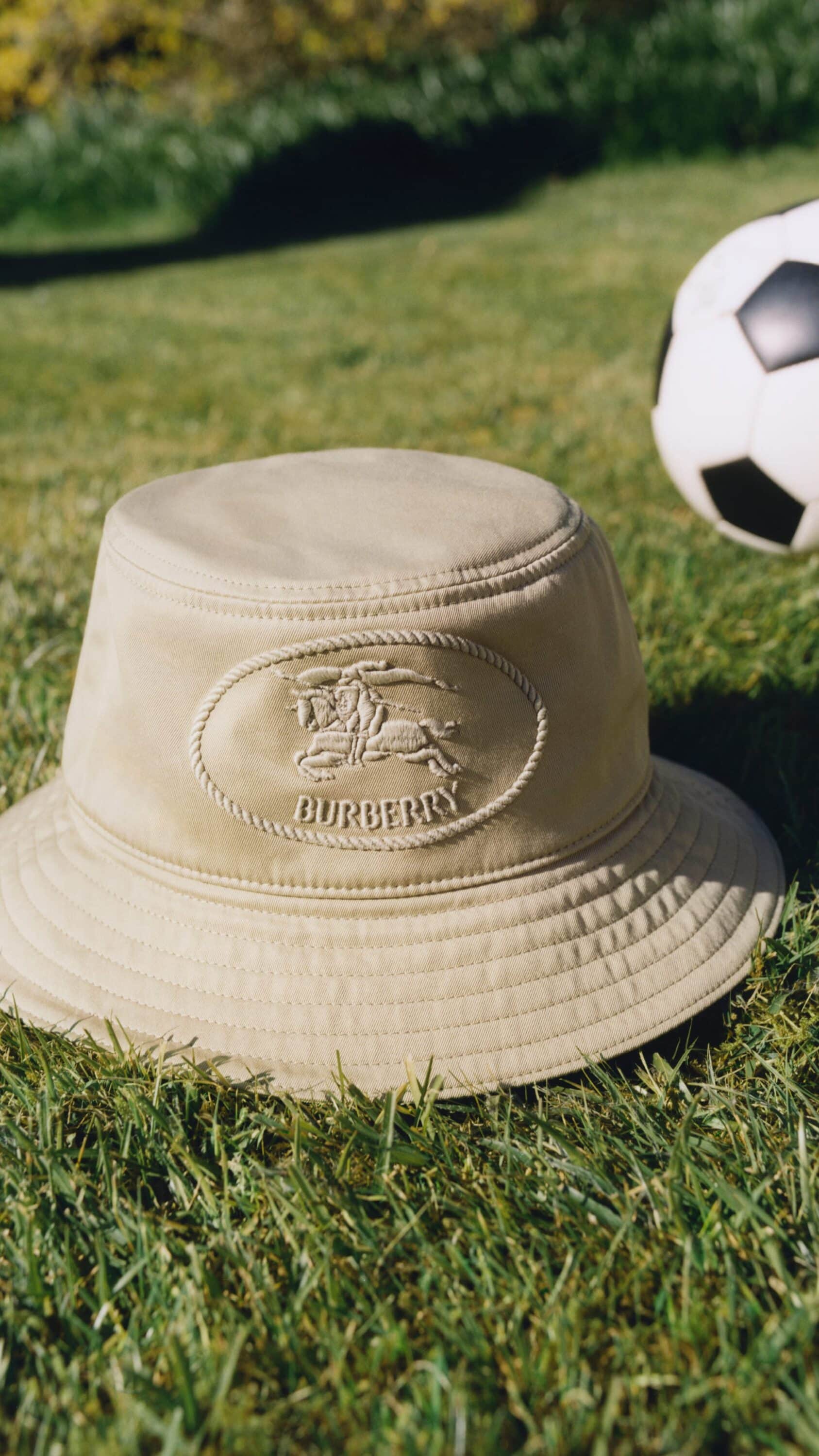 Beige Burberry bucket hat resting on vibrant green grass beside a classic black and white soccer ball