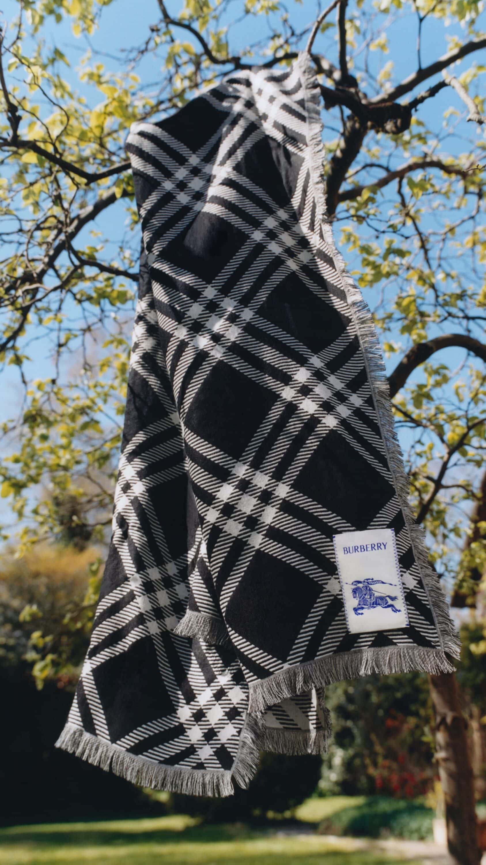 Black and white patterned scarf draped over a tree branch against a clear blue sky and green foliage background