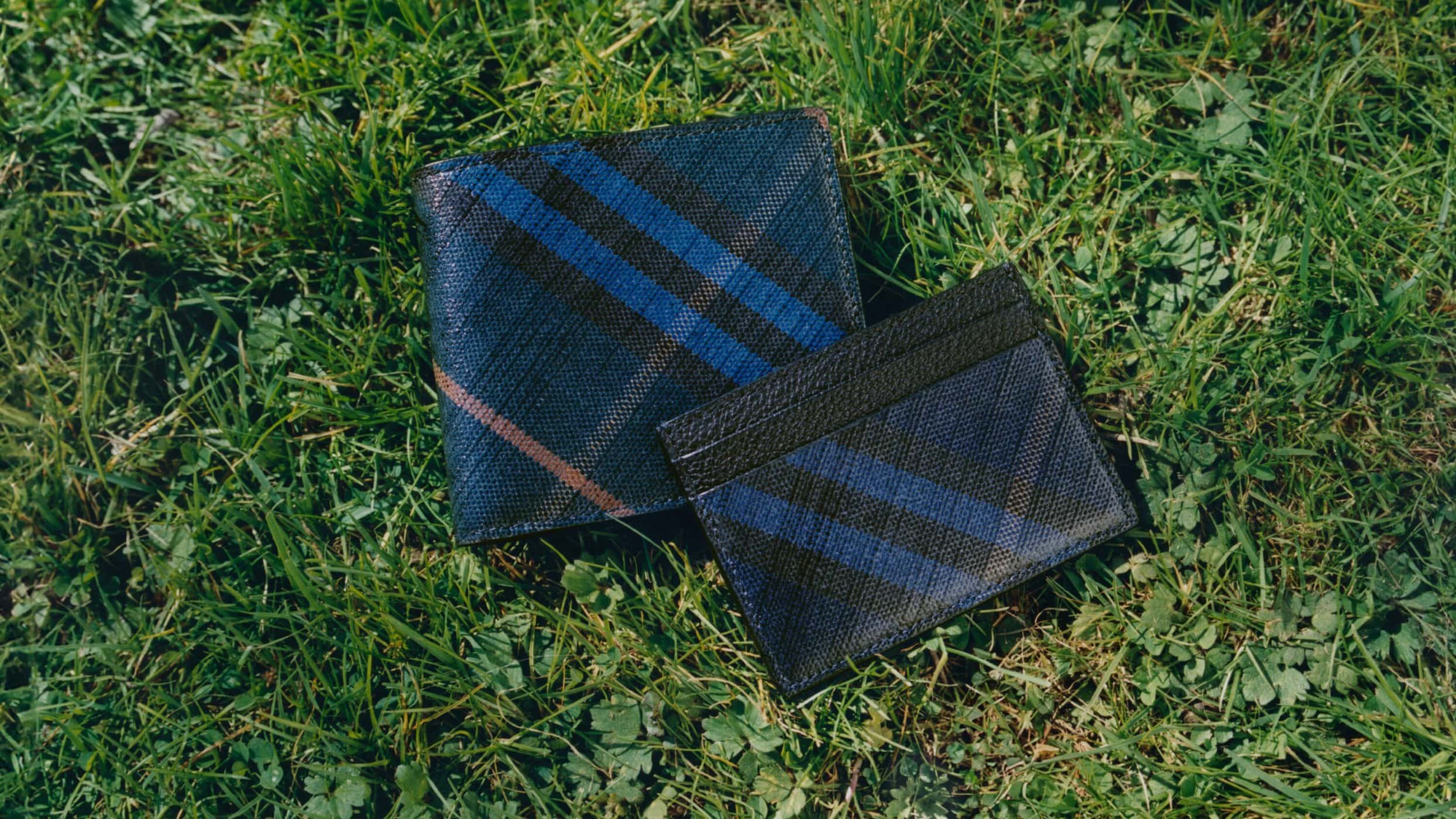 Blue plaid leather wallet and cardholder resting on green grass outdoors for Burberry Father's Day 2025 campaign.