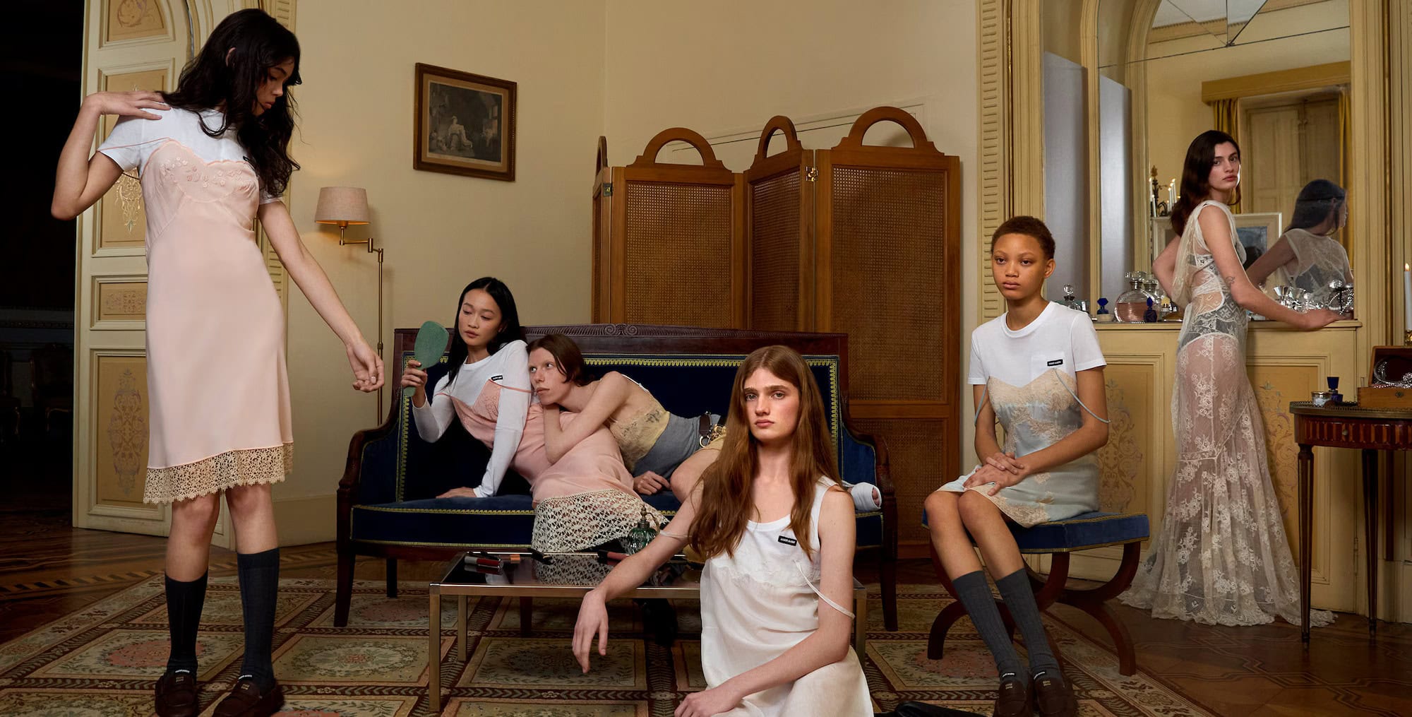 Group of models in layered slip dresses and t-shirts posing in a classic interior with ornate wood furniture and mirrors