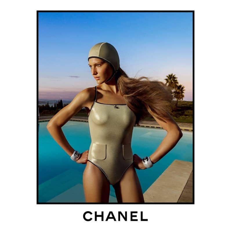Model in metallic swimsuit and matching swim cap standing by a pool at sunset for Chanel Spring 2025 ad campaign.