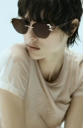 Model wearing dark tinted sunglasses and a light-coloured top against a pale blue background for Blumarine Eyewear 2025.