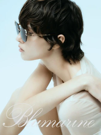 Close-up profile of a model wearing dark sunglasses and a pale top against a light blue background for Blumarine.