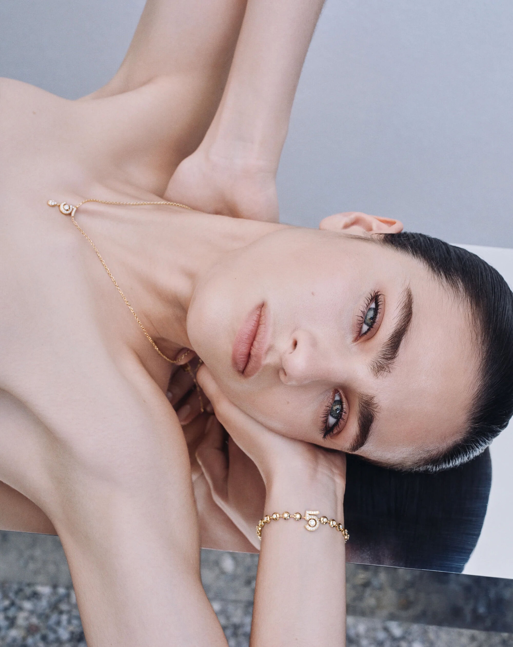 Close-up portrait of a woman wearing fine jewelry including a gold necklace and bracelet featuring a number five charm