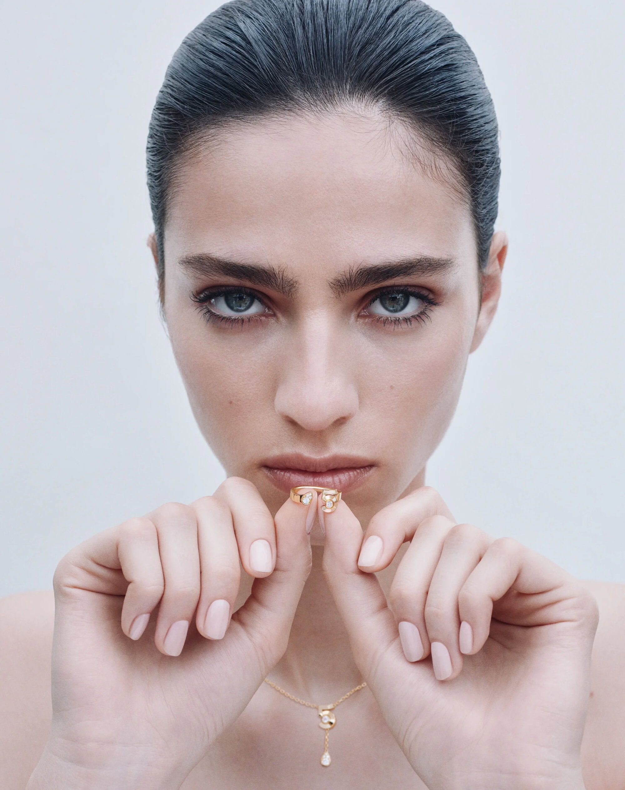 Close-up portrait of a woman holding a gold ring up to her face against a neutral white background for Chanel.