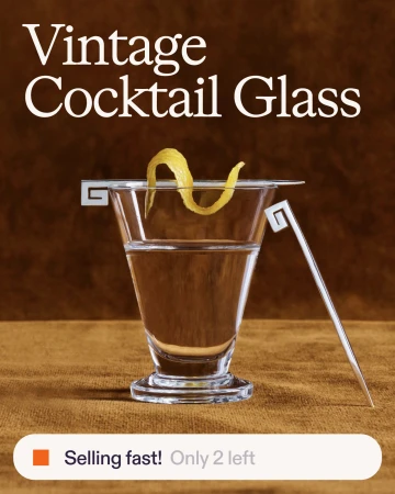 Vintage cocktail glass with a yellow lemon twist garnish and a metal cocktail pick resting on a brown textured surface