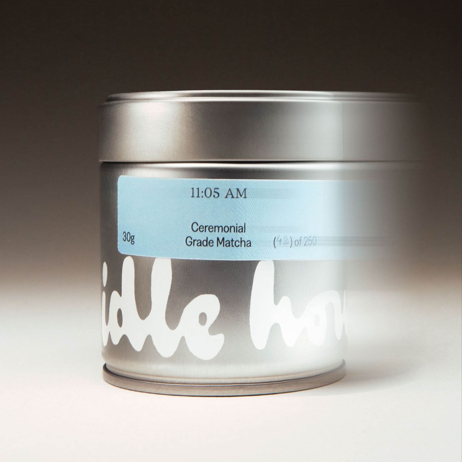 Cylindrical metal tin of ceremonial grade matcha with a blue label and motion blur effect against a neutral background