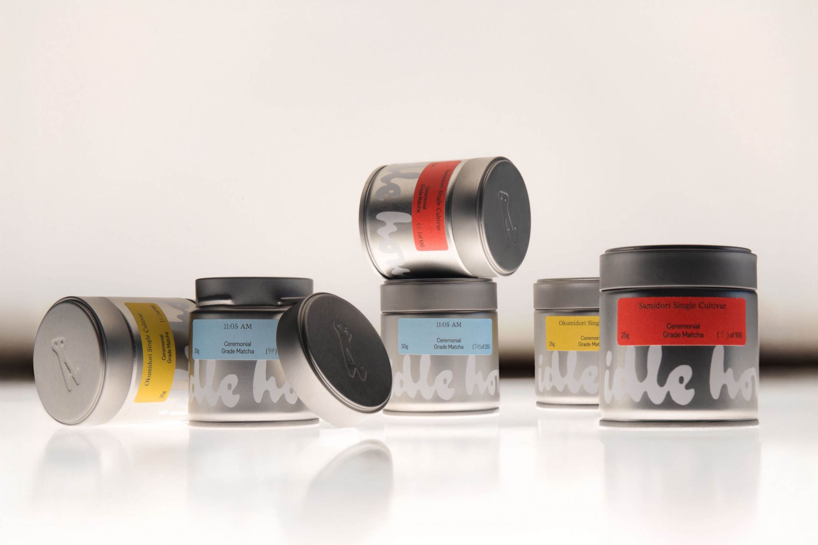 Silver matcha tea tins with colorful labels and branding arranged on a glossy white surface