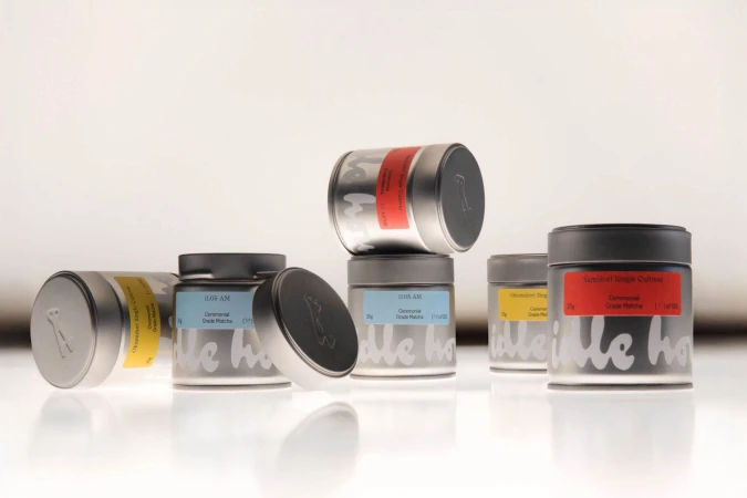 Silver matcha tea tins with colorful labels and branding arranged on a glossy white surface