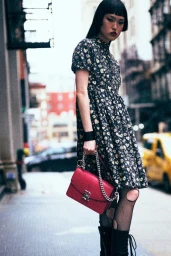 Model in printed dress and fishnet tights holding a red handbag on a city street