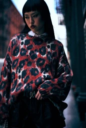 Model with long dark hair wearing a red leopard print distressed sweater outdoors in an urban alleyway