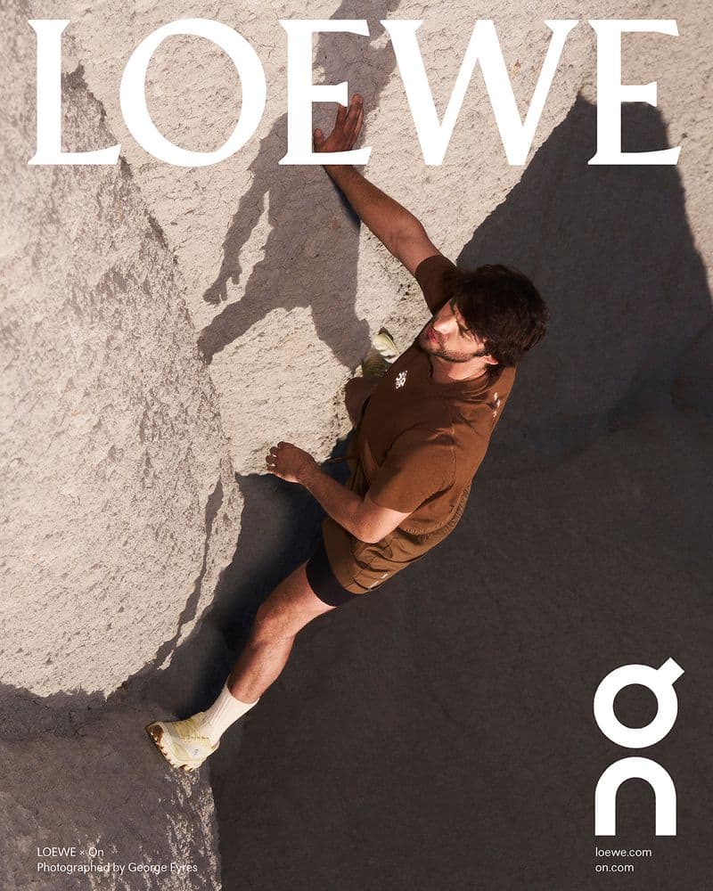 A man wearing a brown t-shirt scaling a rugged rock formation, captured from a high-angle overhead perspective.