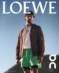 Man wearing a brown zip jacket, white t-shirt, and bright green shorts against a clear blue sky