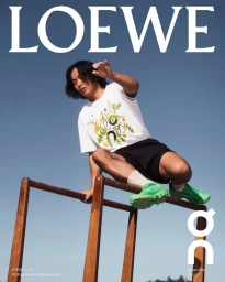Man wearing a white graphic t-shirt and black shorts vaulting over wooden parallel bars against a clear blue sky