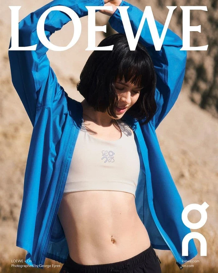 Woman in blue zip jacket and white sports bra stretching arms overhead outdoors
