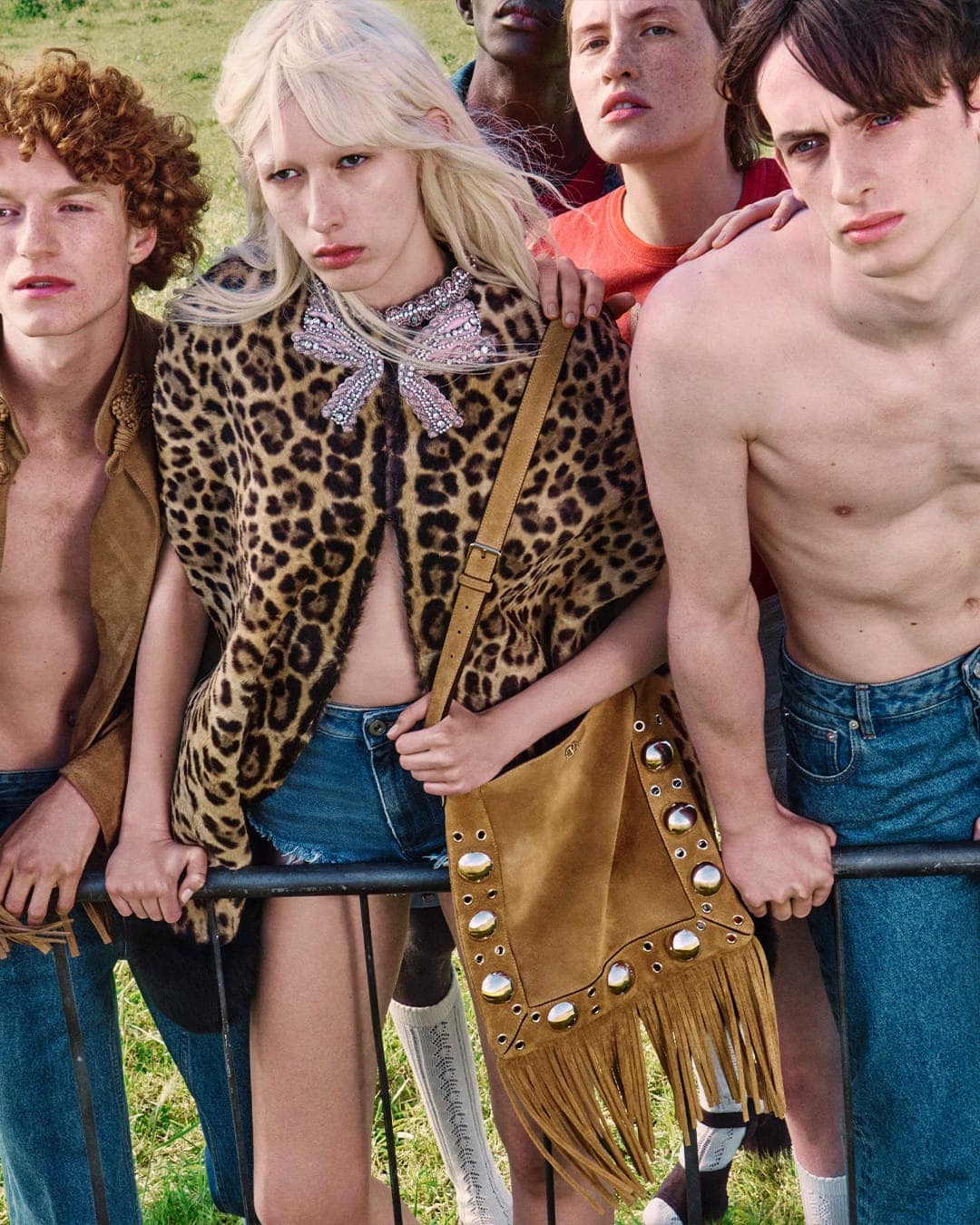 Group of diverse young models posing together outdoors behind a railing for Valentino ad campaign wearing casual clothing and carrying a fringed bag.