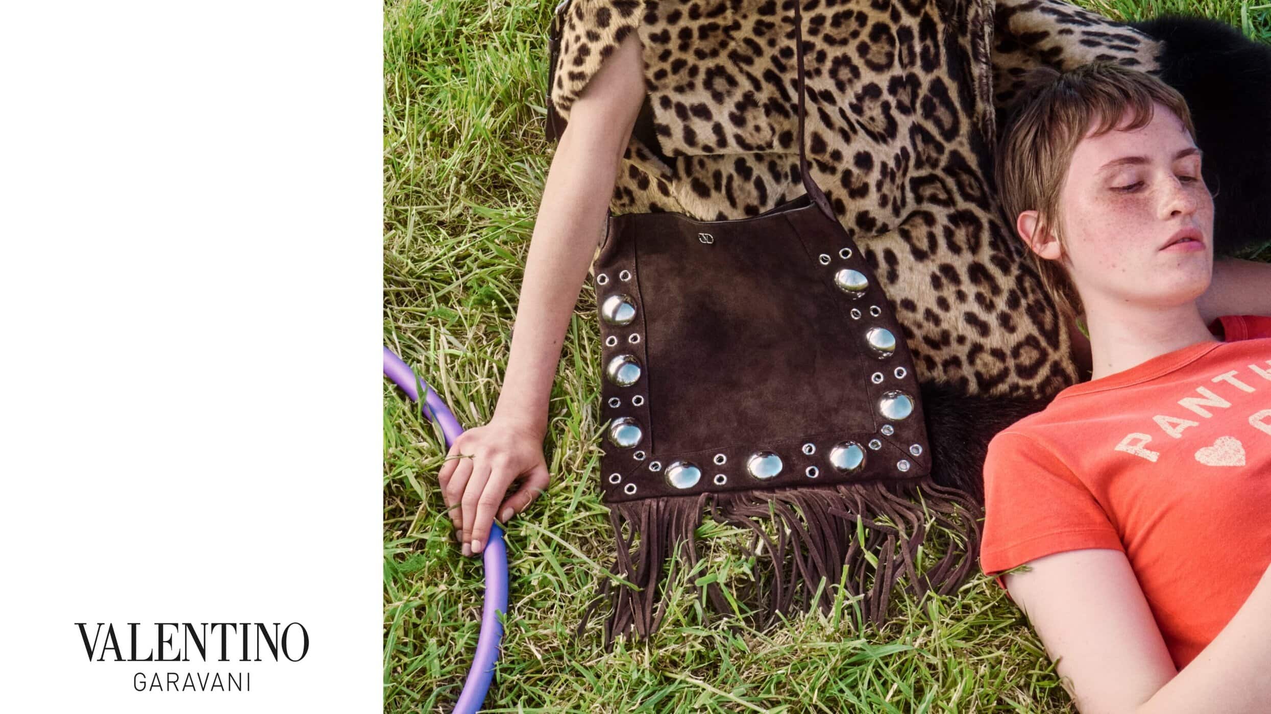 Model lying on grass next to a studded fringed suede bag wearing an orange t-shirt with leopard print apparel nearby