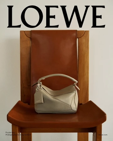 Tan leather Loewe puzzle bag resting on a brown wooden chair against a plain white wall