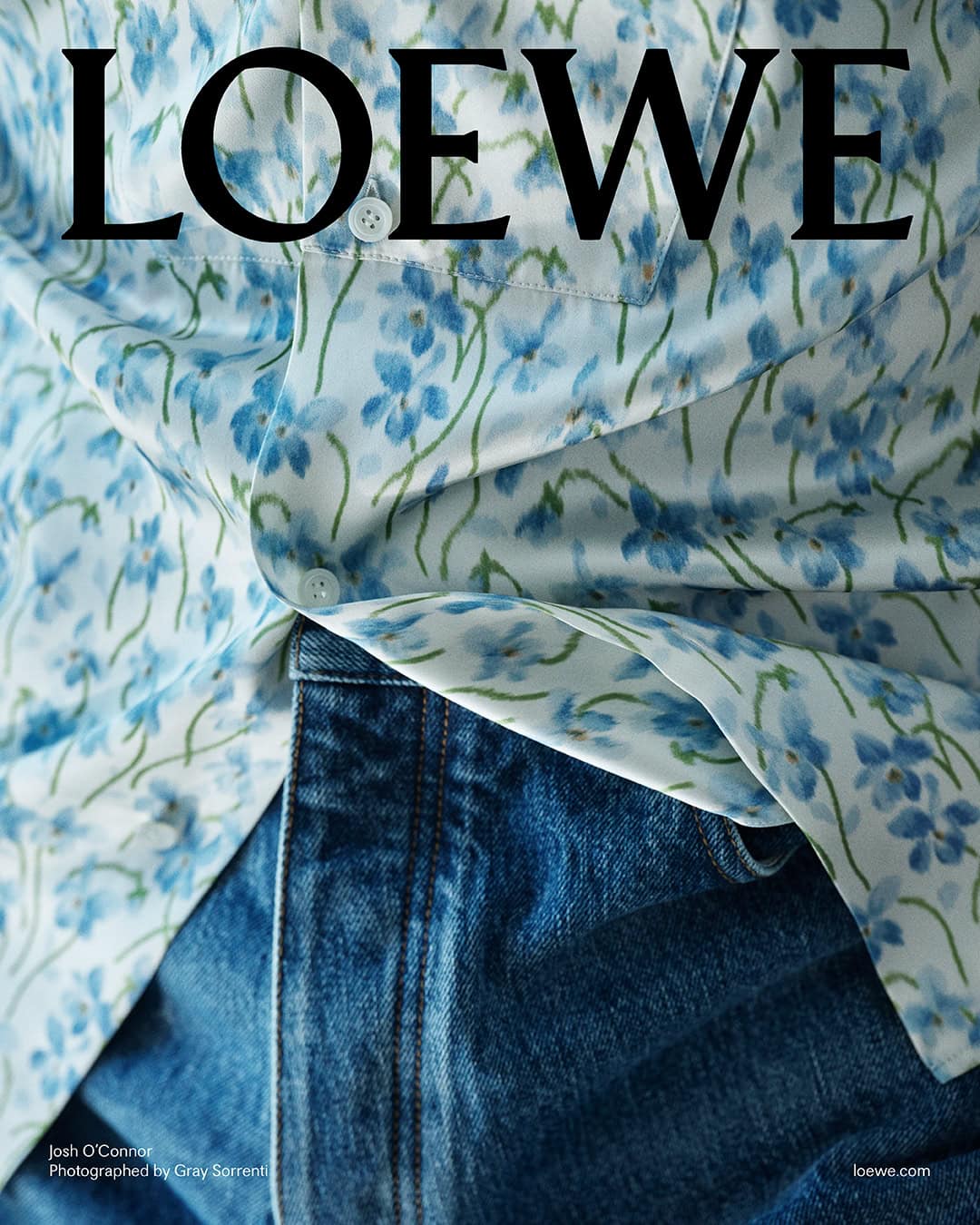 Close-up of a person wearing a light blue floral print button-down shirt tucked into dark denim jeans.