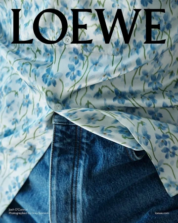 Close-up of a person wearing a light blue floral print button-down shirt tucked into dark denim jeans.