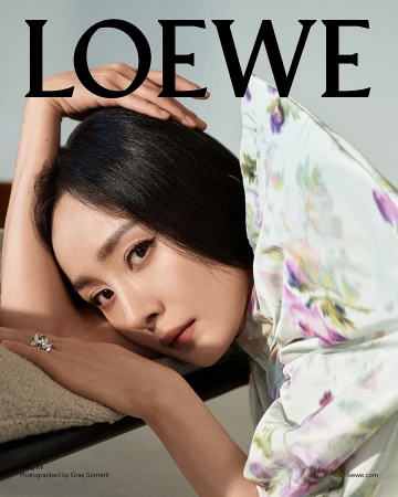 Portrait of Yang Mi wearing a floral printed garment with her hand resting near her head against a plain background