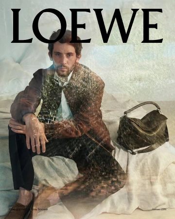 Josh O'Connor seated on a rumpled white textile surface beside a leather handbag, with a double exposure effect.