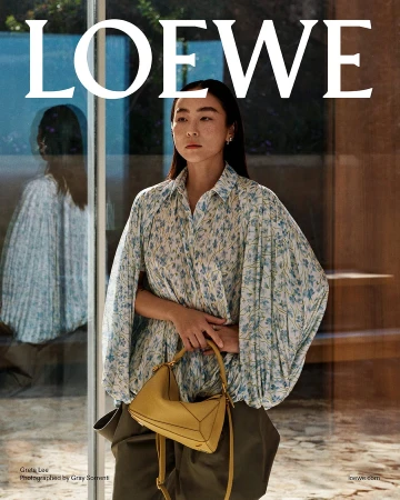 Greta Lee wearing a blue floral blouse and olive trousers holding a yellow handbag for Loewe
