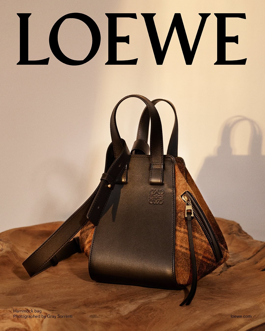 Loewe Hammock handbag resting on a dark wood surface against a neutral wall for the Pre-Fall 2025 ad campaign.