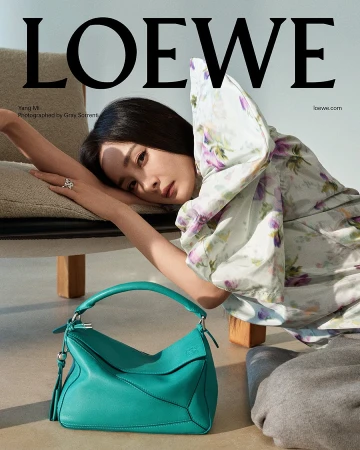 Yang Mi leaning against a modern upholstered chair beside a teal leather bag for Loewe Pre-Fall 2025 campaign.