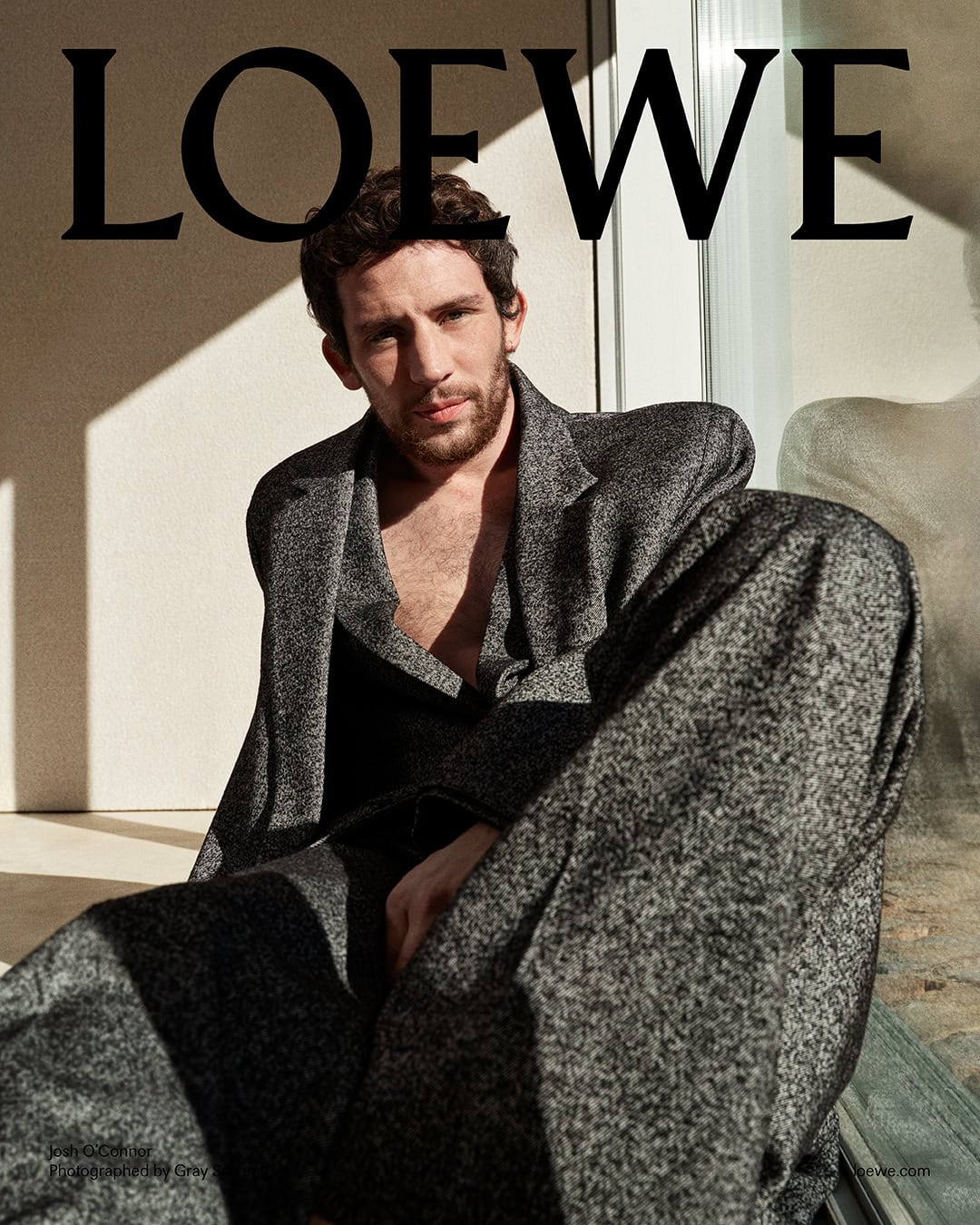 Josh O'Connor in a textured grey blazer and trousers against a neutral wall for Loewe Pre-Fall 2025 campaign photographed by Gray Sorrenti