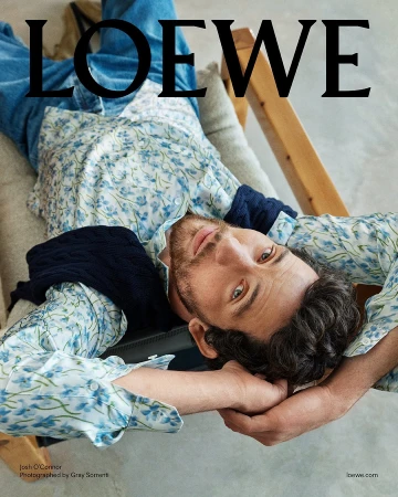 Josh O Connor reclining in a wooden armchair wearing a blue floral shirt for the Loewe Pre Fall 2025 campaign photographed by Gray Sorrenti
