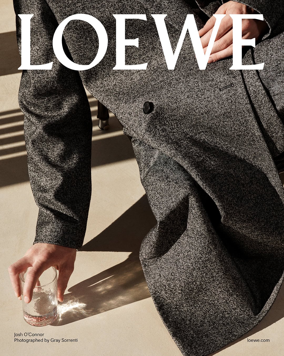Close-up of Josh O'Connor in a textured grey wool coat holding a glass of water, photographed by Gray Sorrenti for Loewe Pre-Fall 2025.