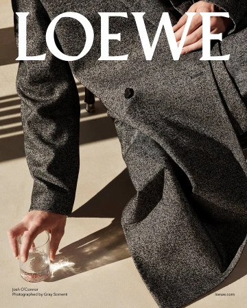 Close-up of Josh O'Connor in a textured grey wool coat holding a glass of water, photographed by Gray Sorrenti for Loewe Pre-Fall 2025.