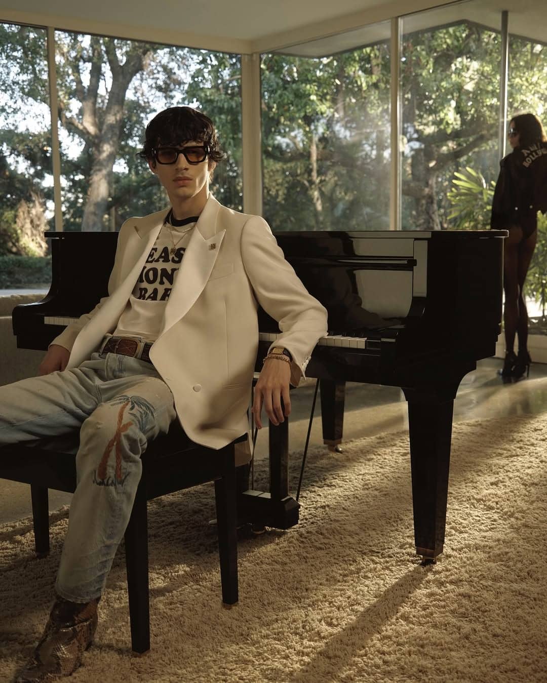 Man in cream blazer and patterned jeans seated at a black grand piano in a modern interior