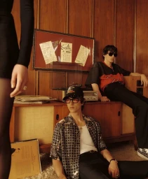 Two young male models in retro attire relaxing inside a wood-paneled room for Amiri Pre-Fall 2025 campaign.