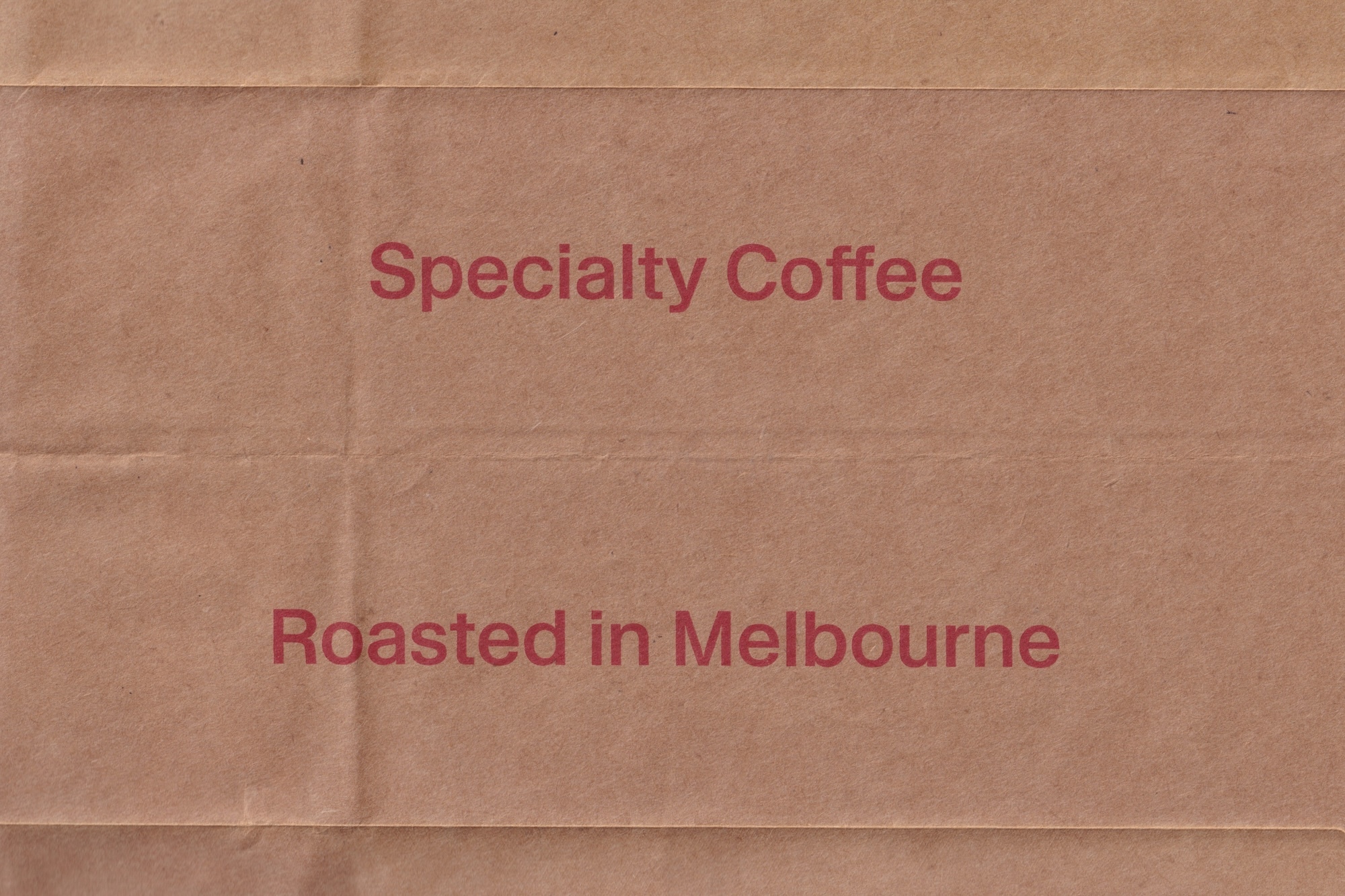 Brown kraft paper texture featuring red printed text reading Specialty Coffee and Roasted in Melbourne.