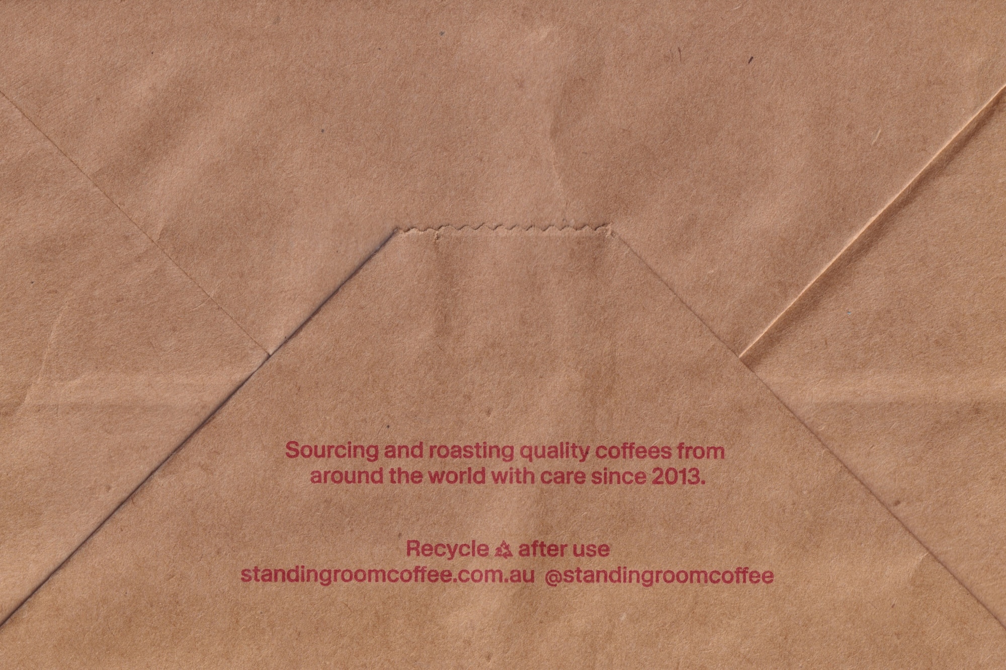 Brown craft paper texture with creased folds and printed red text detailing coffee sourcing and recycling info.